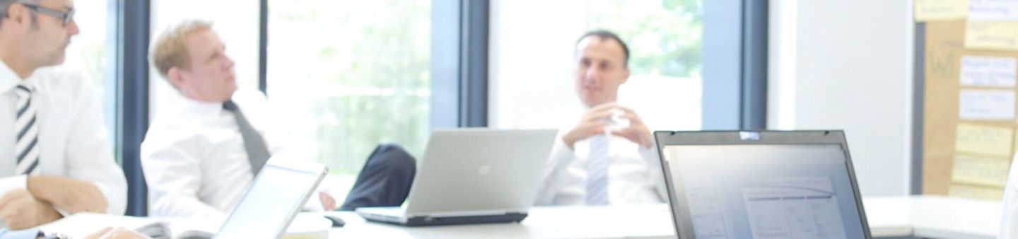 Geschäftsmänner sitzen in einem Konferenzraum mit Laptops.